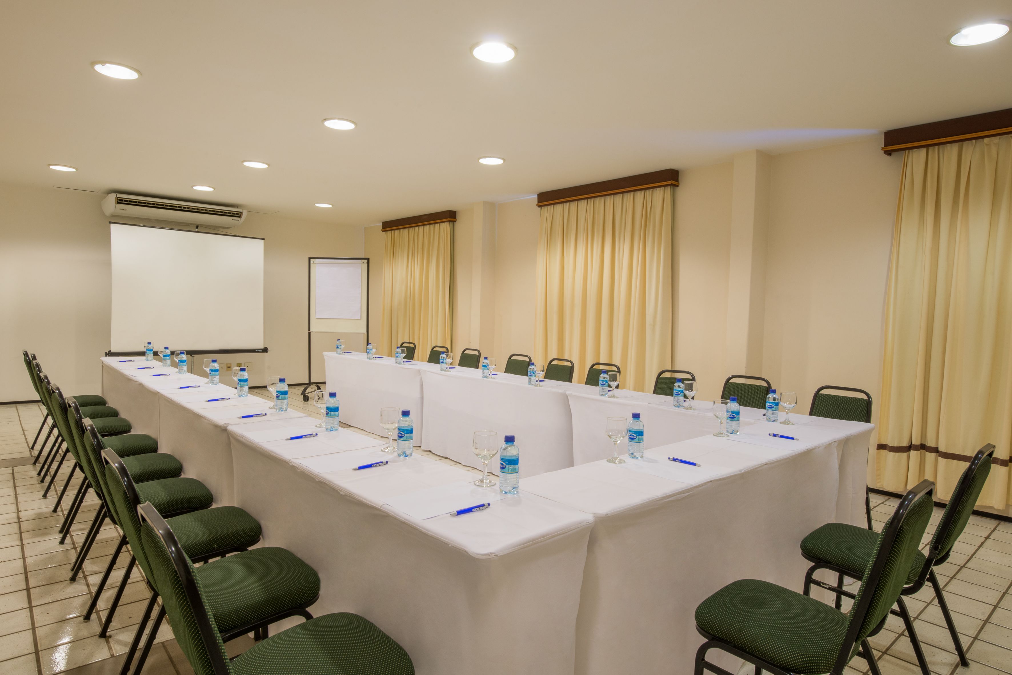 Un salón de conferencias con una larga mesa, sillas, botellas de agua y una pantalla para proyector.
