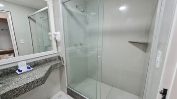 A modern bathroom with a granite countertop, a glass shower enclosure, and a mirror with a mounted hairdryer.