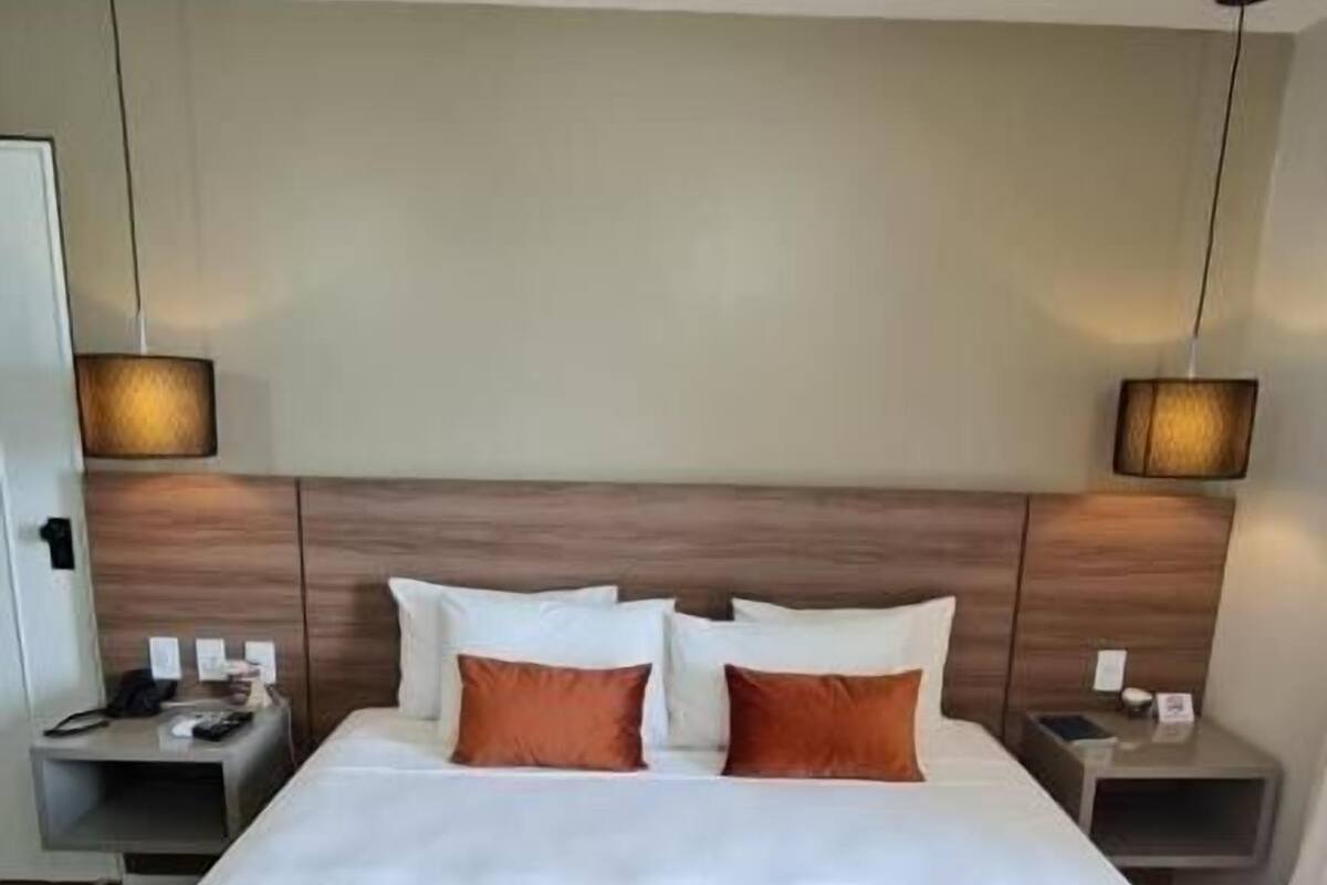 A hotel room with a large bed, two nightstands, a wooden headboard, and wall-mounted lamps.