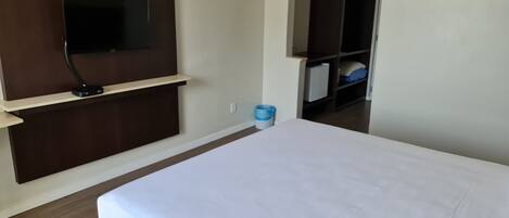 A hotel room with a bed, a TV mounted on the wall, a wardrobe, and a trash bin.