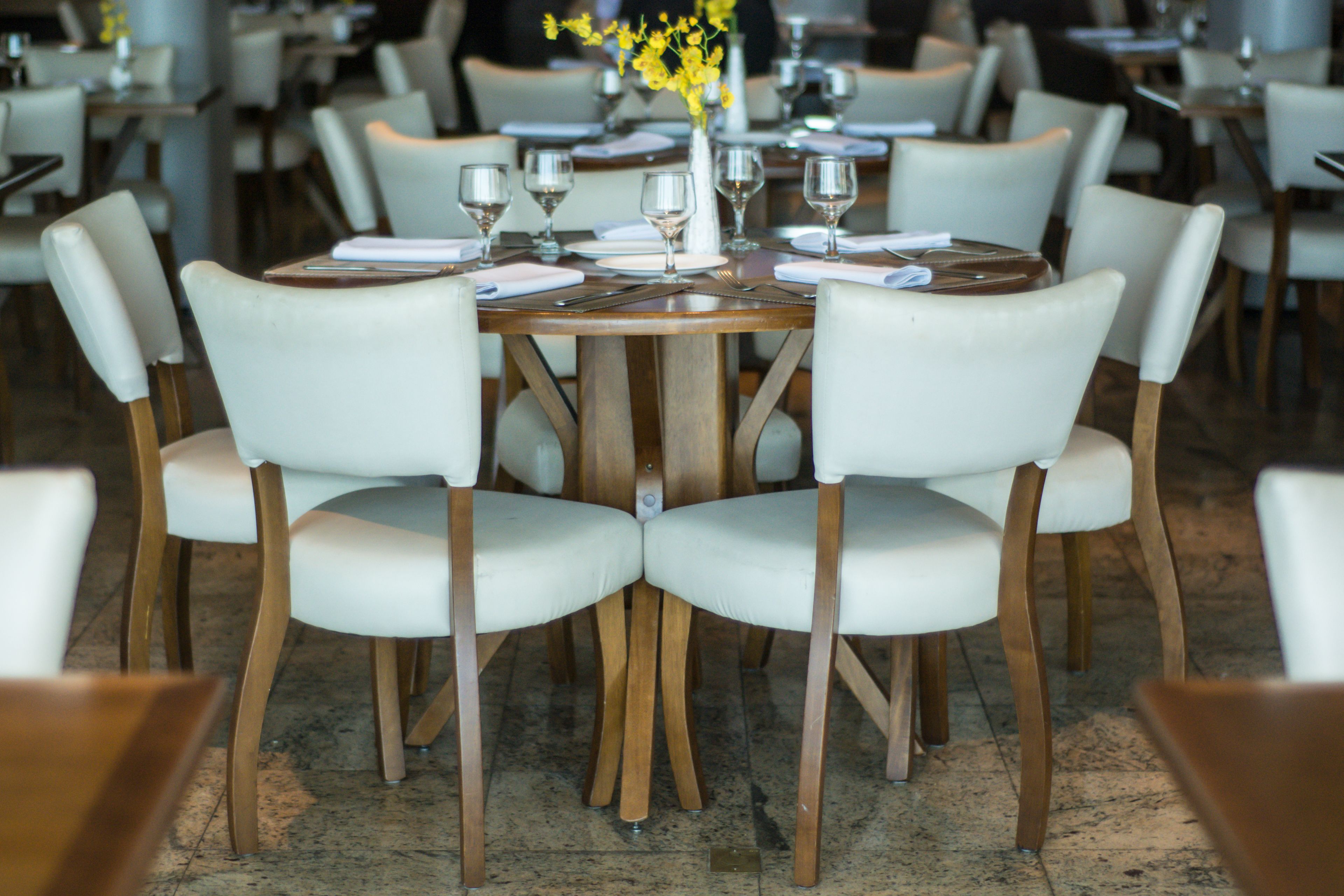 Un espace repas avec des tables rondes, des chaises à revêtement blanc et un vase rempli de fleurs jaunes.