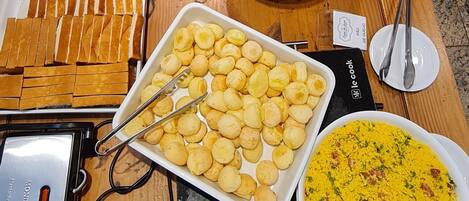 A buffet table with various dishes including pastries, bread, and a yellow rice dish.