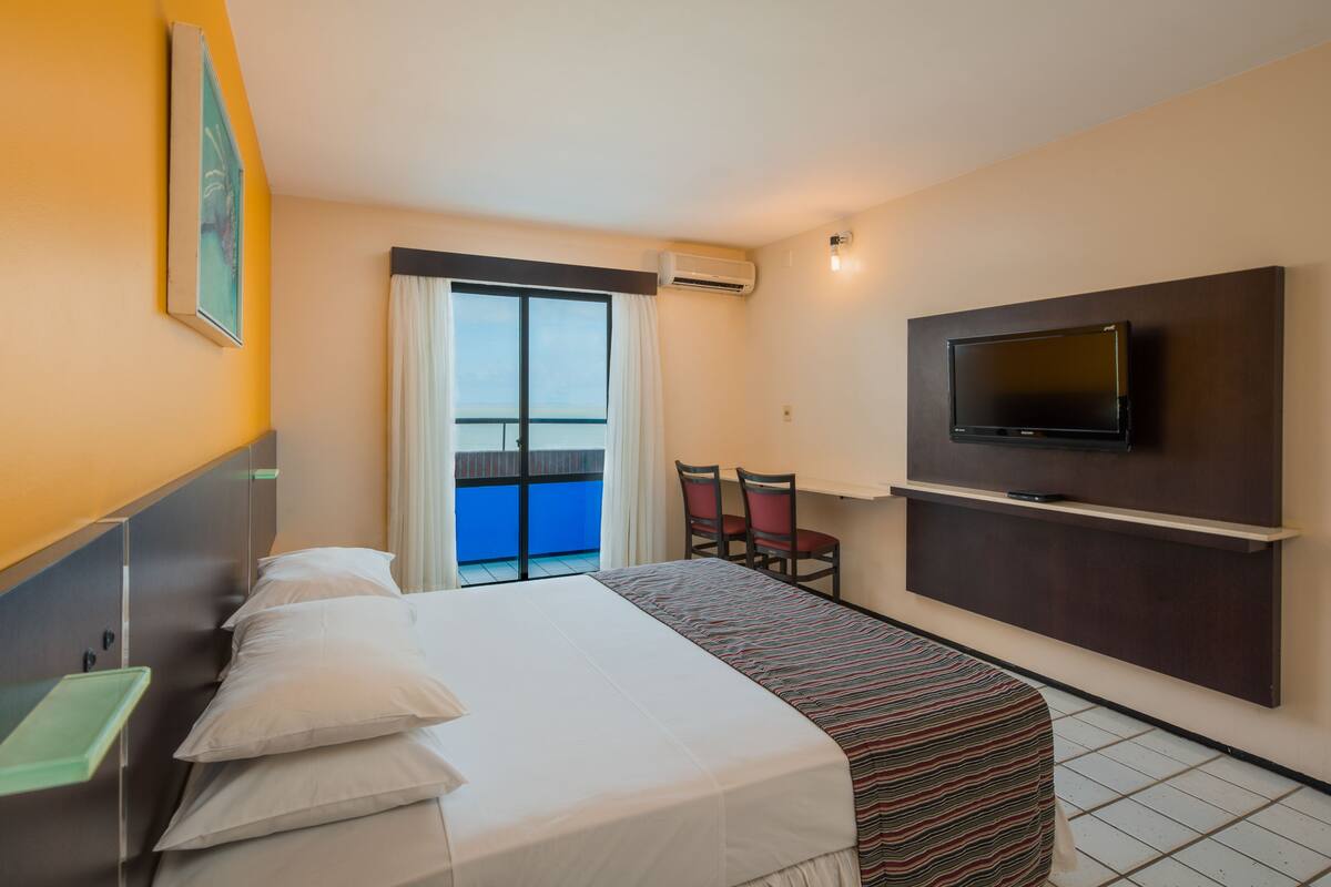 A hotel room with a bed, a TV mounted on the wall, a small table, and a chair.