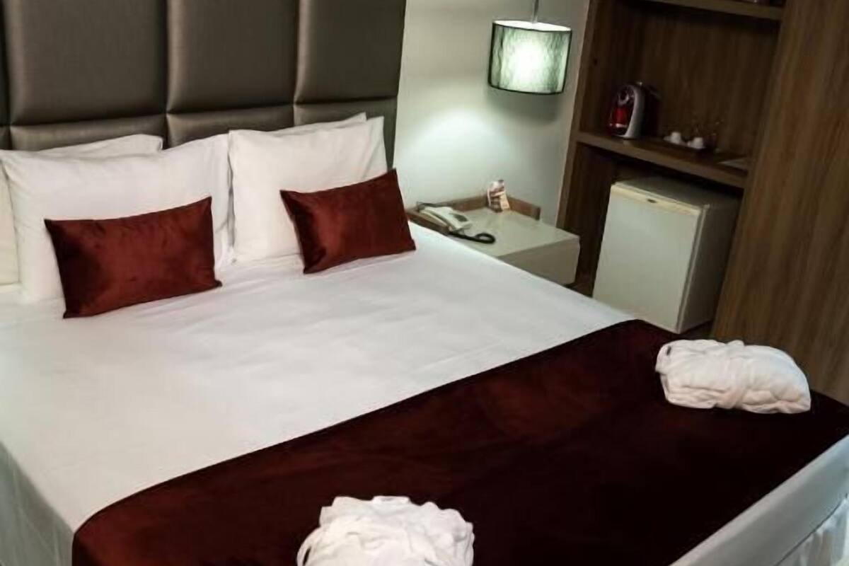 A hotel room with a large bed, a wooden headboard, a bedside table with a lamp, and a small cabinet.