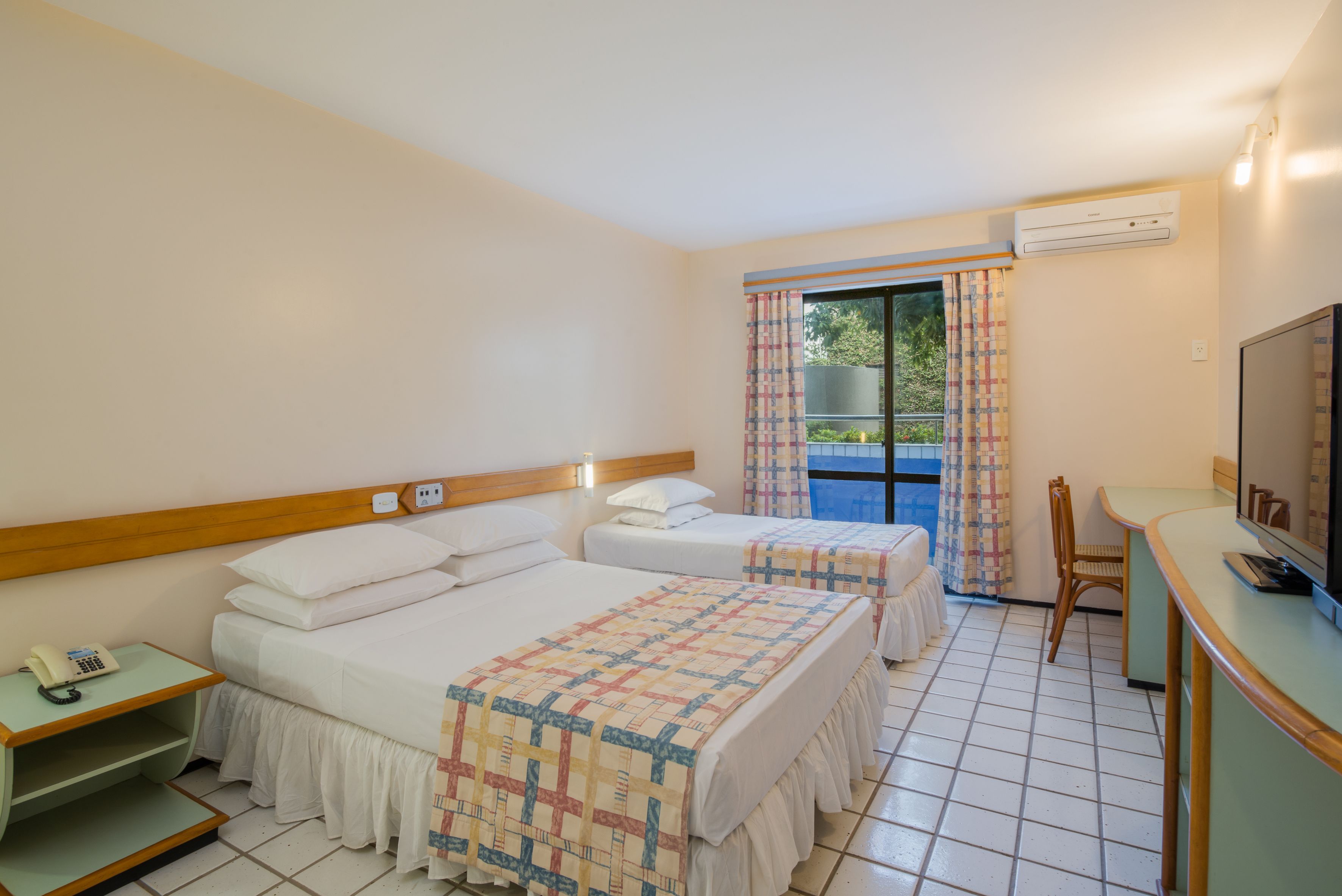 A hotel room with two beds, a desk with a computer, a chair, and an air conditioning unit.