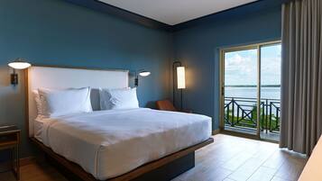 A modern bedroom with a large bed, two bedside tables, and a view of the sea through a balcony.