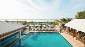 Un espace piscine doté de chaises longues et de parasols, avec vue sur une étendue d’eau.