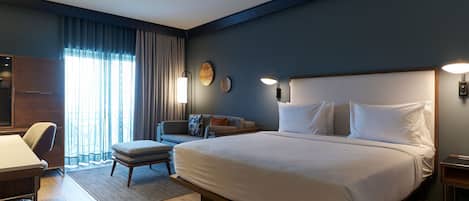A modern hotel room with a large bed, a desk, a chair, and a sofa.