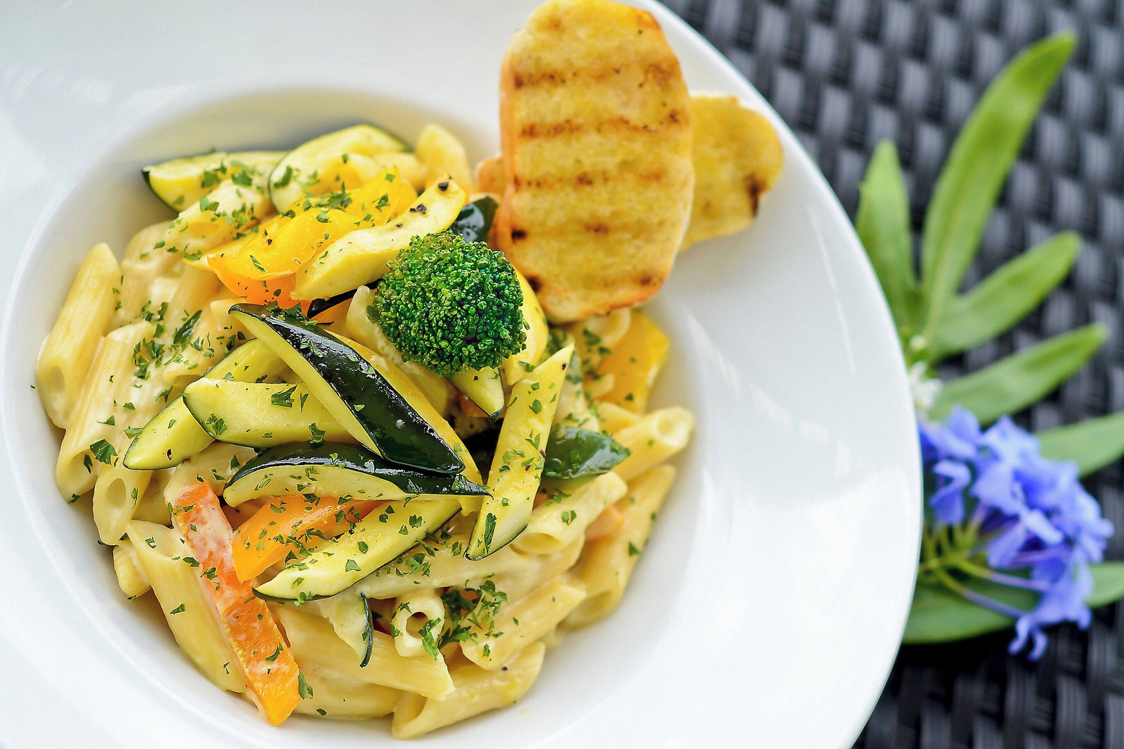 Un plato de pasta con vegetales y una rebanada de pan.