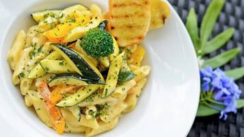Un plato de pasta con vegetales y una rebanada de pan.