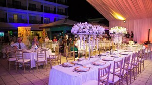 Une salle de banquet avec de longues tables dressées pour un événement formel, agrémentée de nappes blanches et de compositions florales.