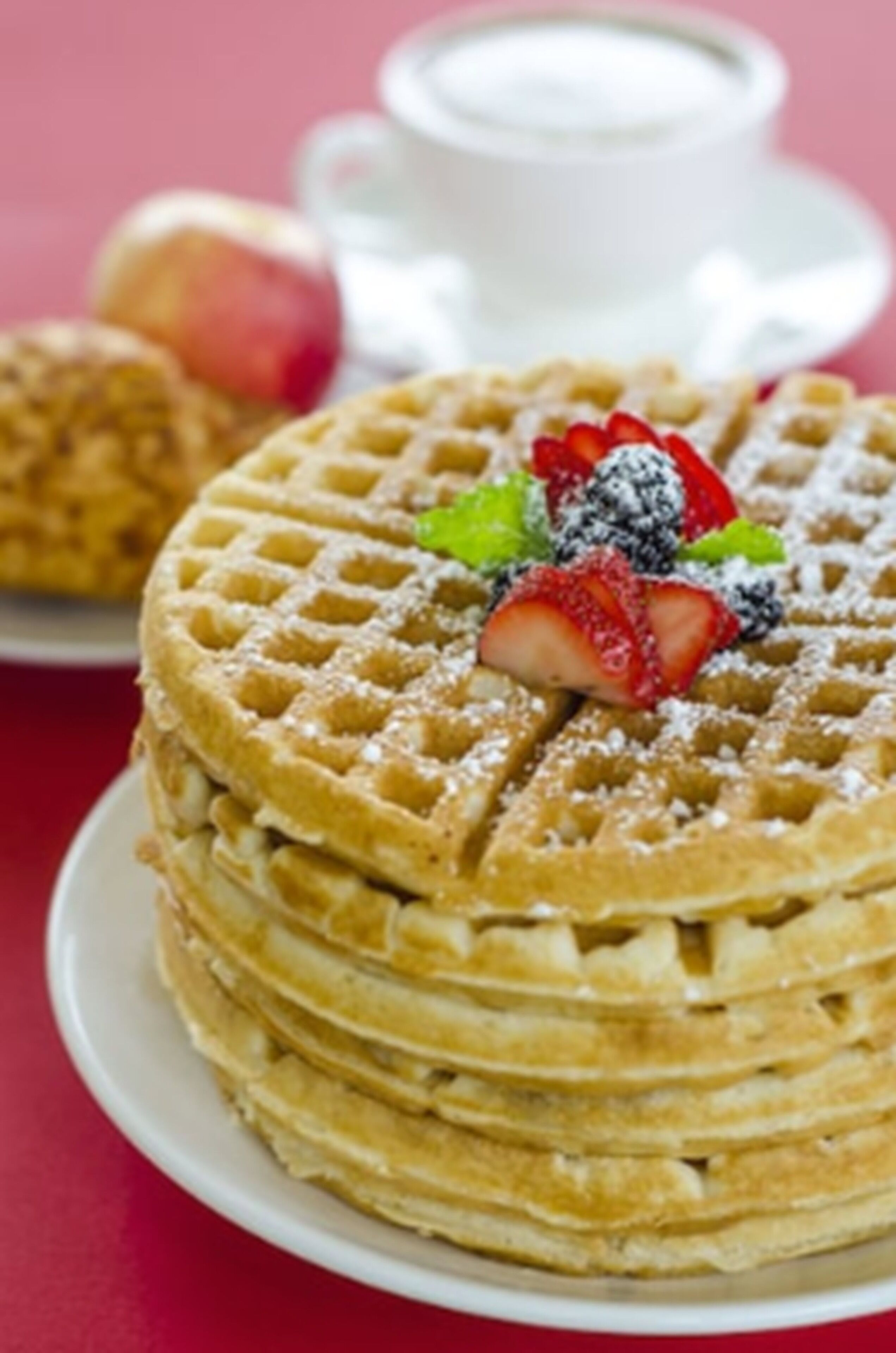 Uma pilha de waffles com morangos e amoras sobre um prato branco.