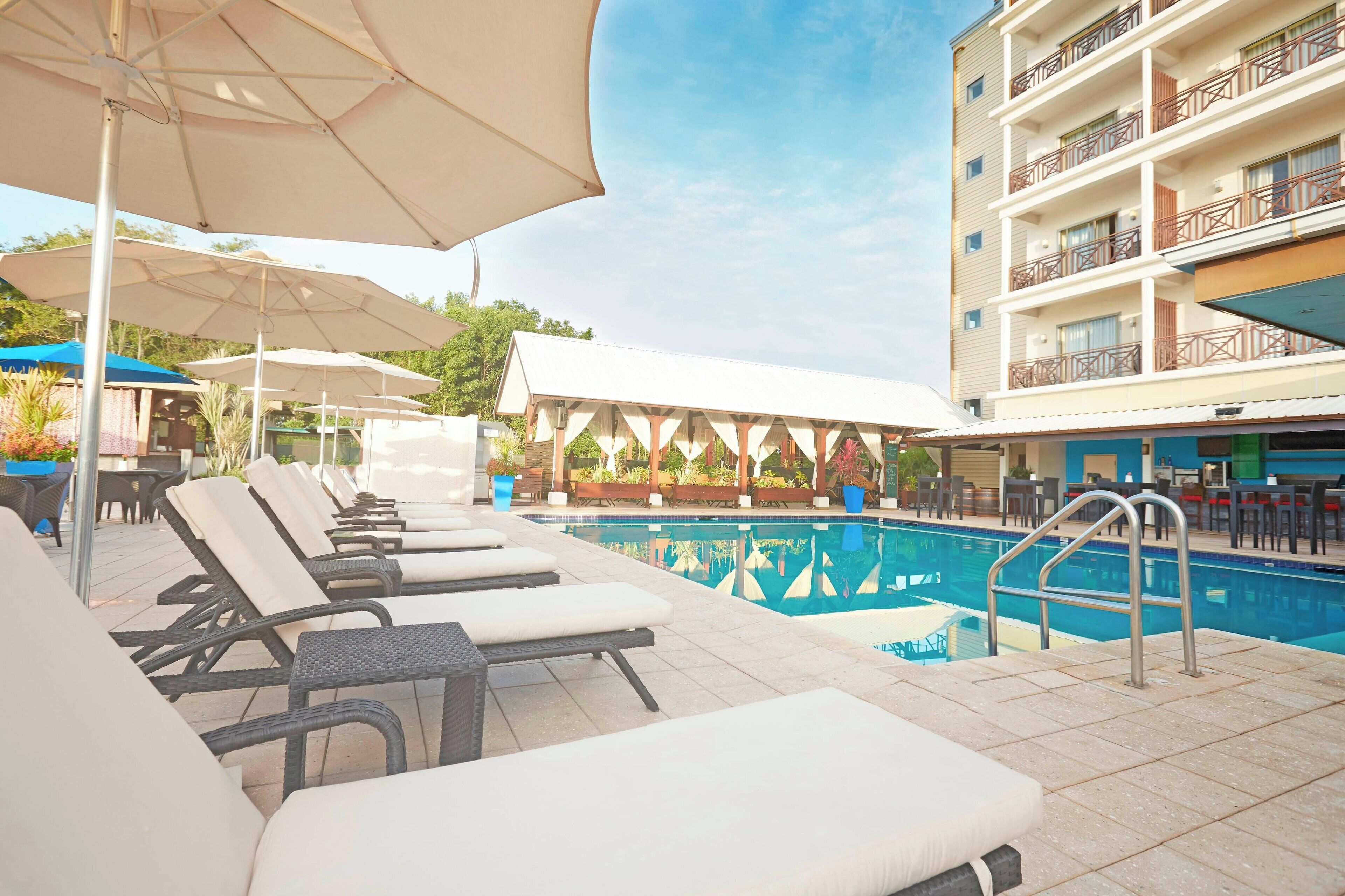 A poolside area with lounge chairs and umbrellas, a pool, and a building with balconies.