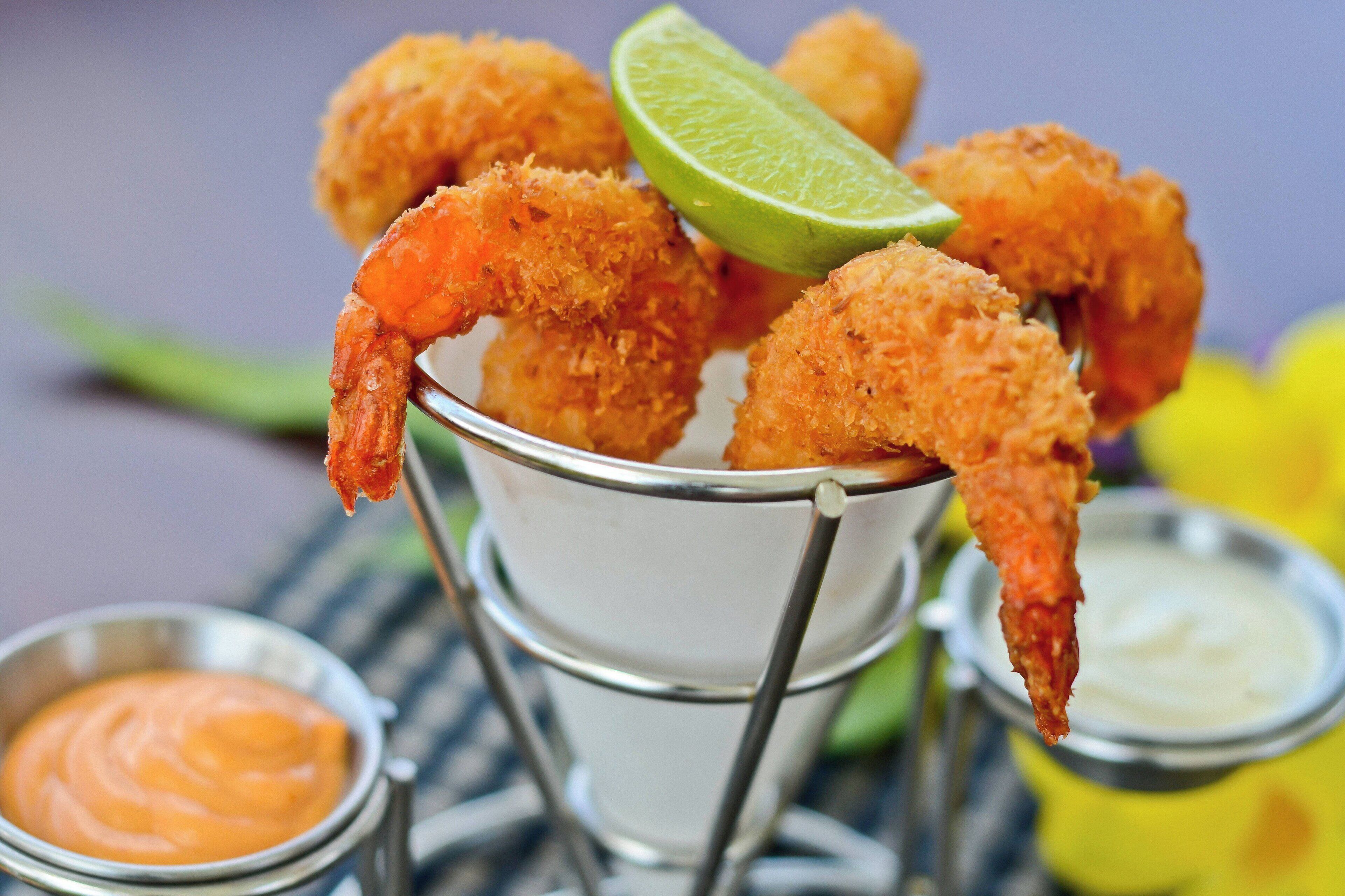 Una cesta metálica con camarones empanizados, un gajo de lima y dos recipientes pequeños de salsas para mojar.