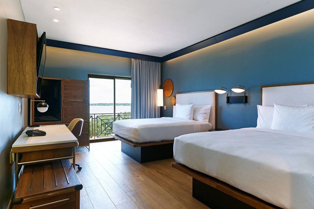 Habitación de hotel con dos camas, un escritorio, una silla, un televisor y vistas al exterior.