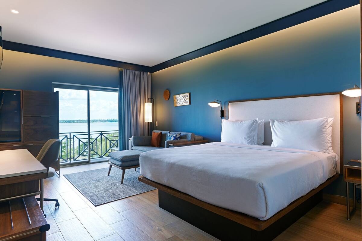 A modern hotel room with a large bed, a desk, and a view of the outdoors.