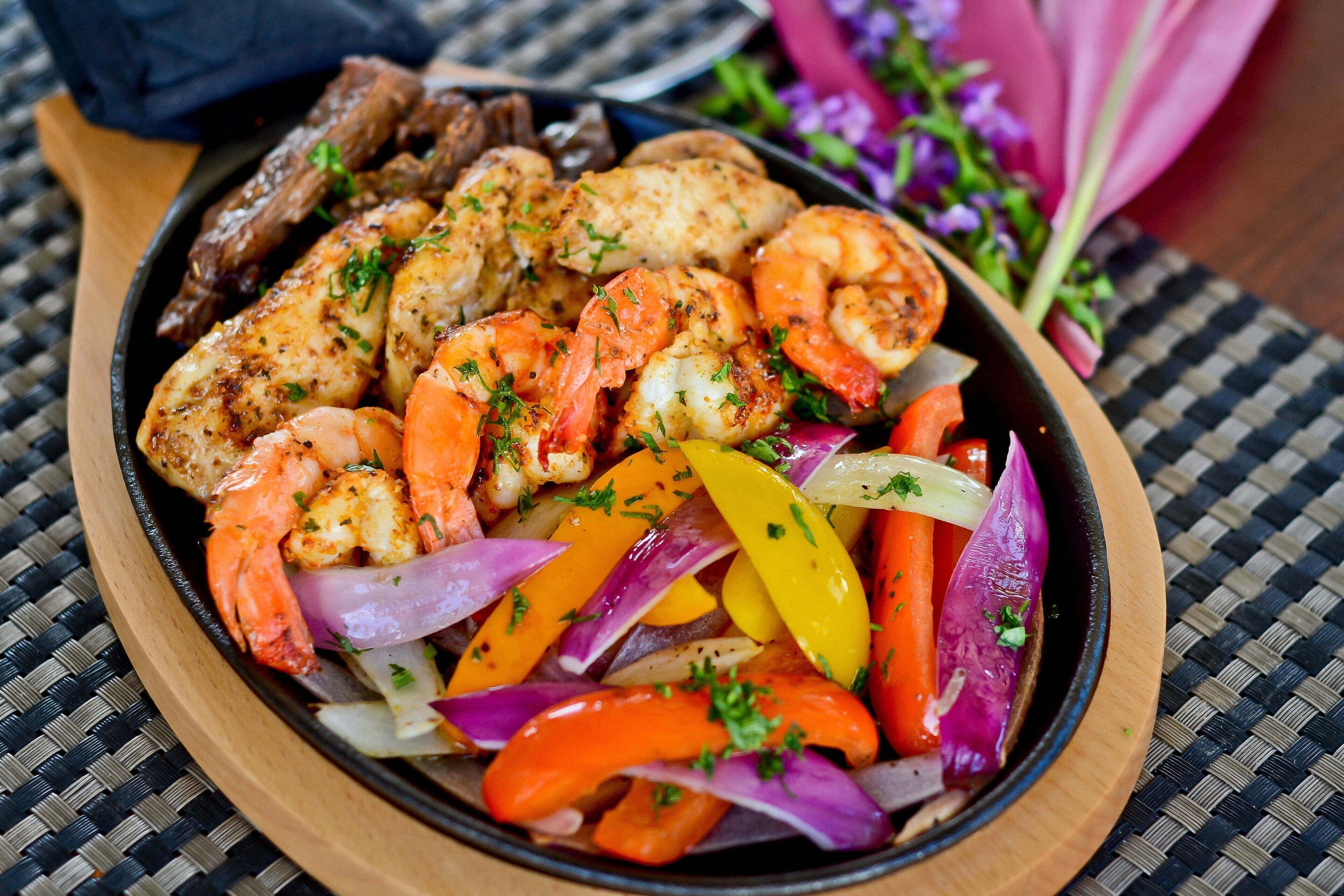 A dish with shrimp, chicken, and vegetables on a wooden board.