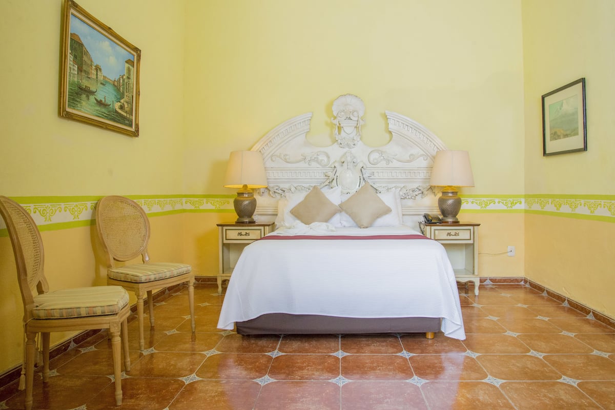 A hotel room with a large bed, two bedside tables, a chair, and a painting on the wall.