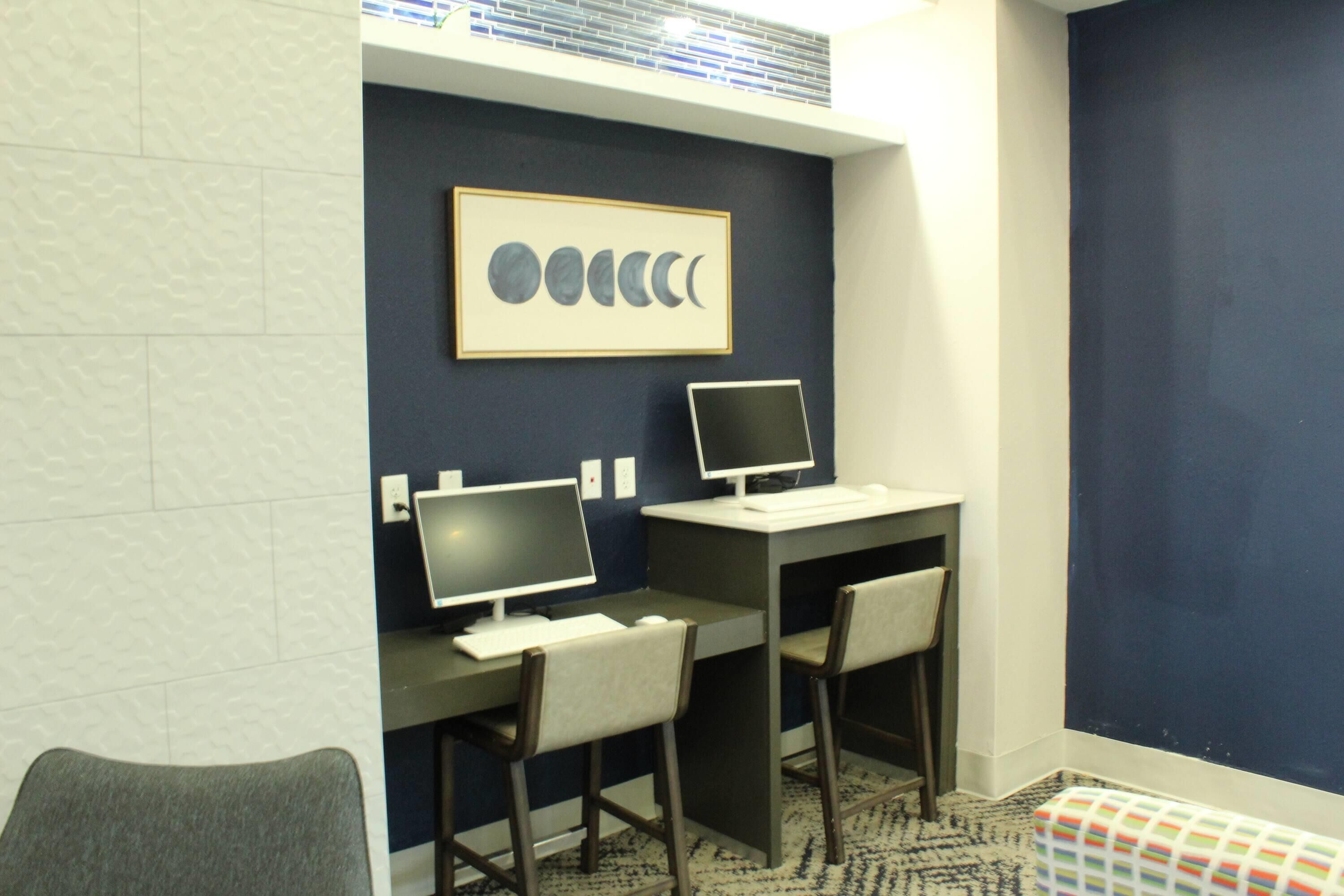 A room with two desks, two chairs, a framed picture of moon phases, and a patterned rug.