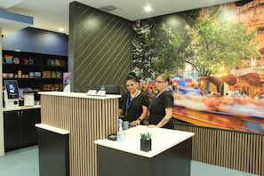 A reception desk with a digital kiosk, a counter with a water bottle, and a mural of a cityscape. -  La Quinta Inn and Suites by Wyndham Schertz-San Antonio-Selma (Schertz)
