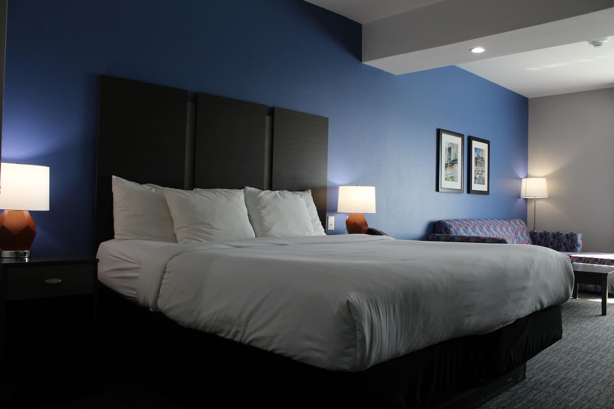 Ein Hotelzimmer mit einem großen Bett, zwei Nachttischen mit Lampen, einem kleinen Tisch mit einem Stuhl und zwei gerahmten Bildern an der Wand.