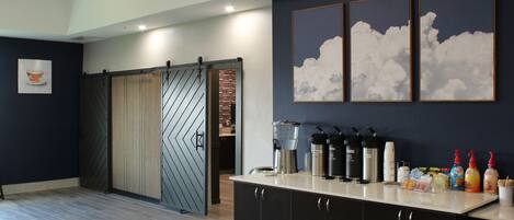 A modern kitchen with a sliding door, a coffee station, and a wall with framed cloud artwork.