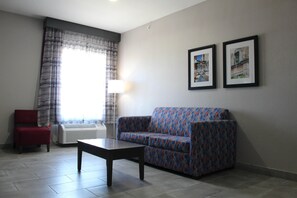 A living room with a patterned sofa, a red chair, a table, and two framed pictures on the wall. -  La Quinta Inn and Suites by Wyndham Schertz-San Antonio-Selma (Schertz)