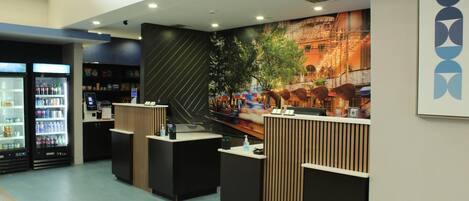 Una zona de recepción con mostrador, dispensador de bebidas y un mural en la pared.