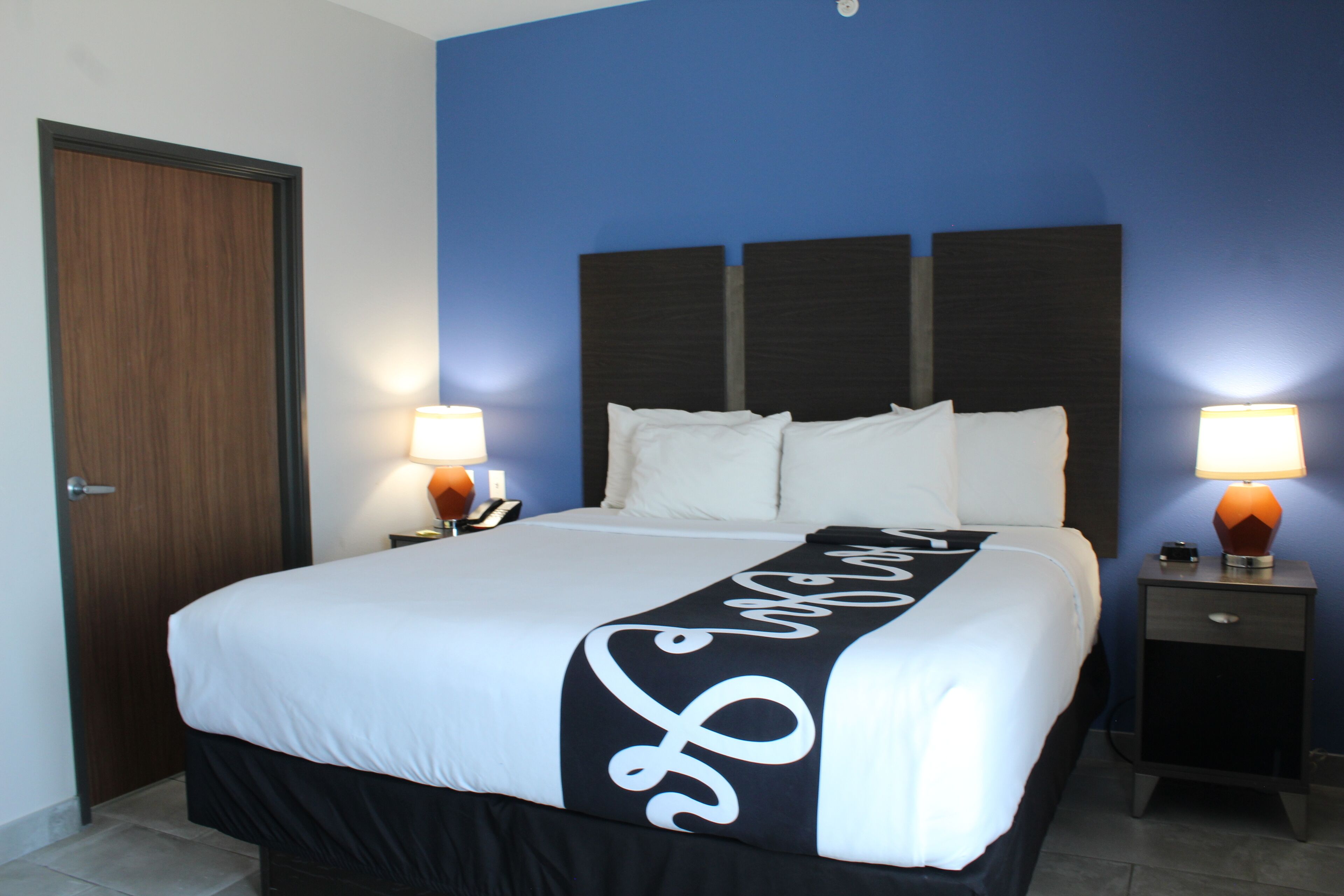 Une chambre d’hôtel avec un grand lit, deux lampes de chevet, une porte en bois et un mur d’accent bleu.