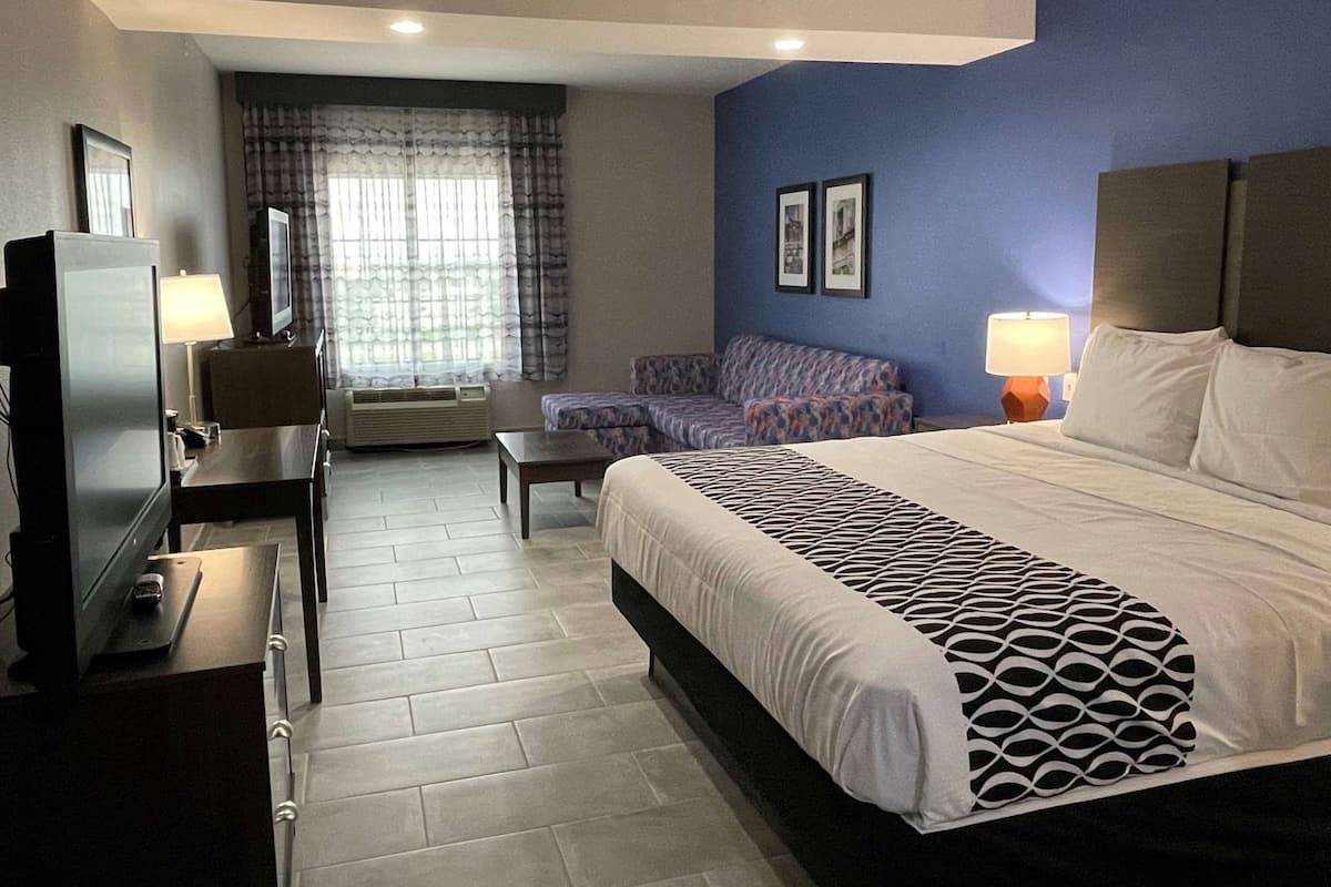 Ein Hotelzimmer mit Bett, Schreibtisch mit Fernseher, Sofa, Sessel und einem Fenster mit Vorhängen.