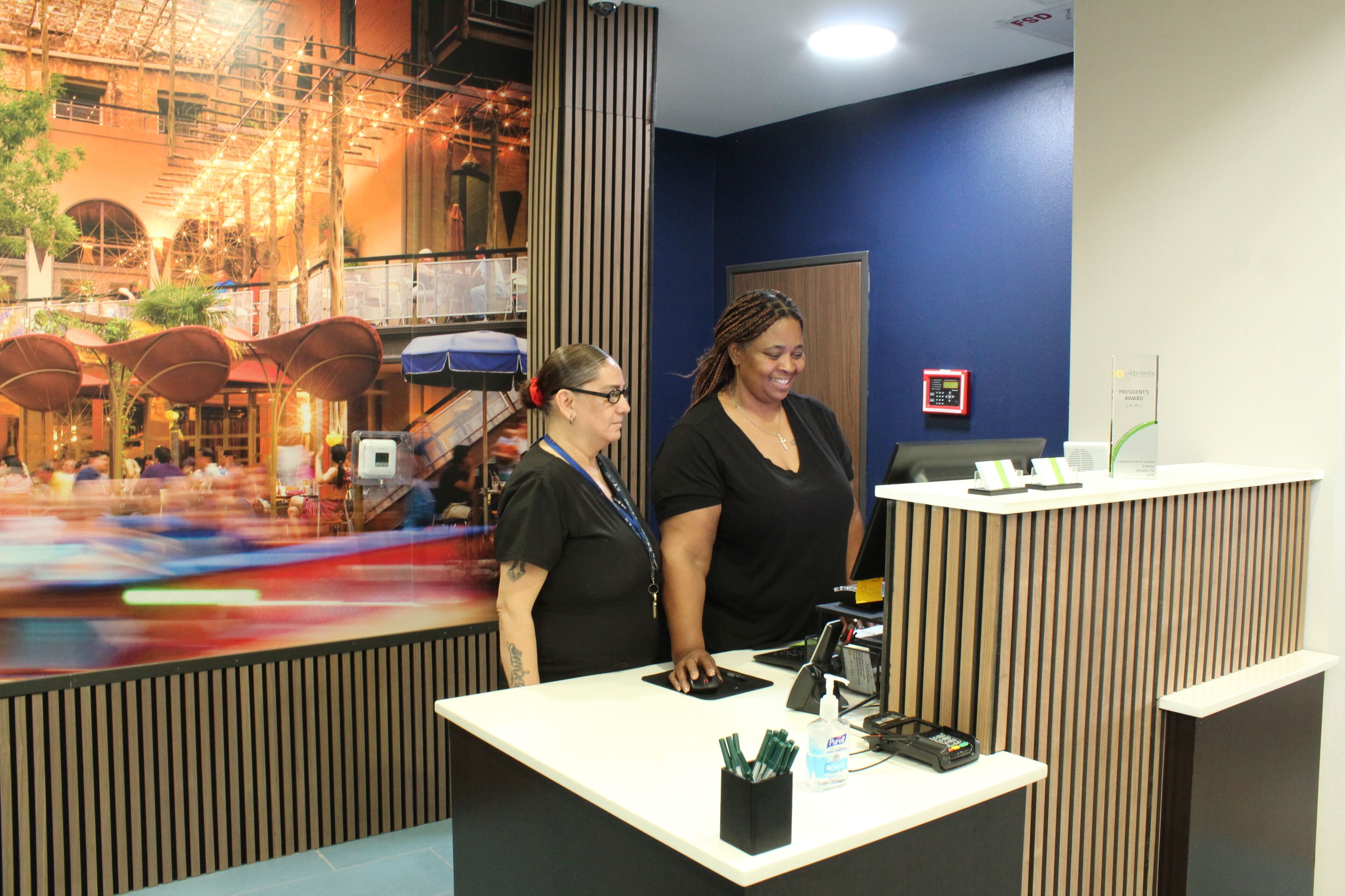 A reception desk with a blue wall, a wooden panel design, and a digital screen.