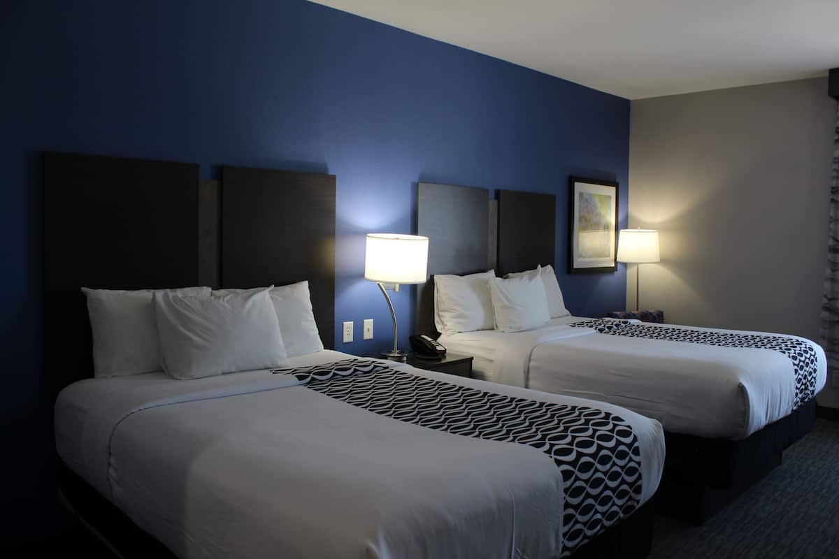 Ein Hotelzimmer mit zwei Betten, jeweils mit Kopfteil, Nachttischlampen und einem Bild an der Wand.