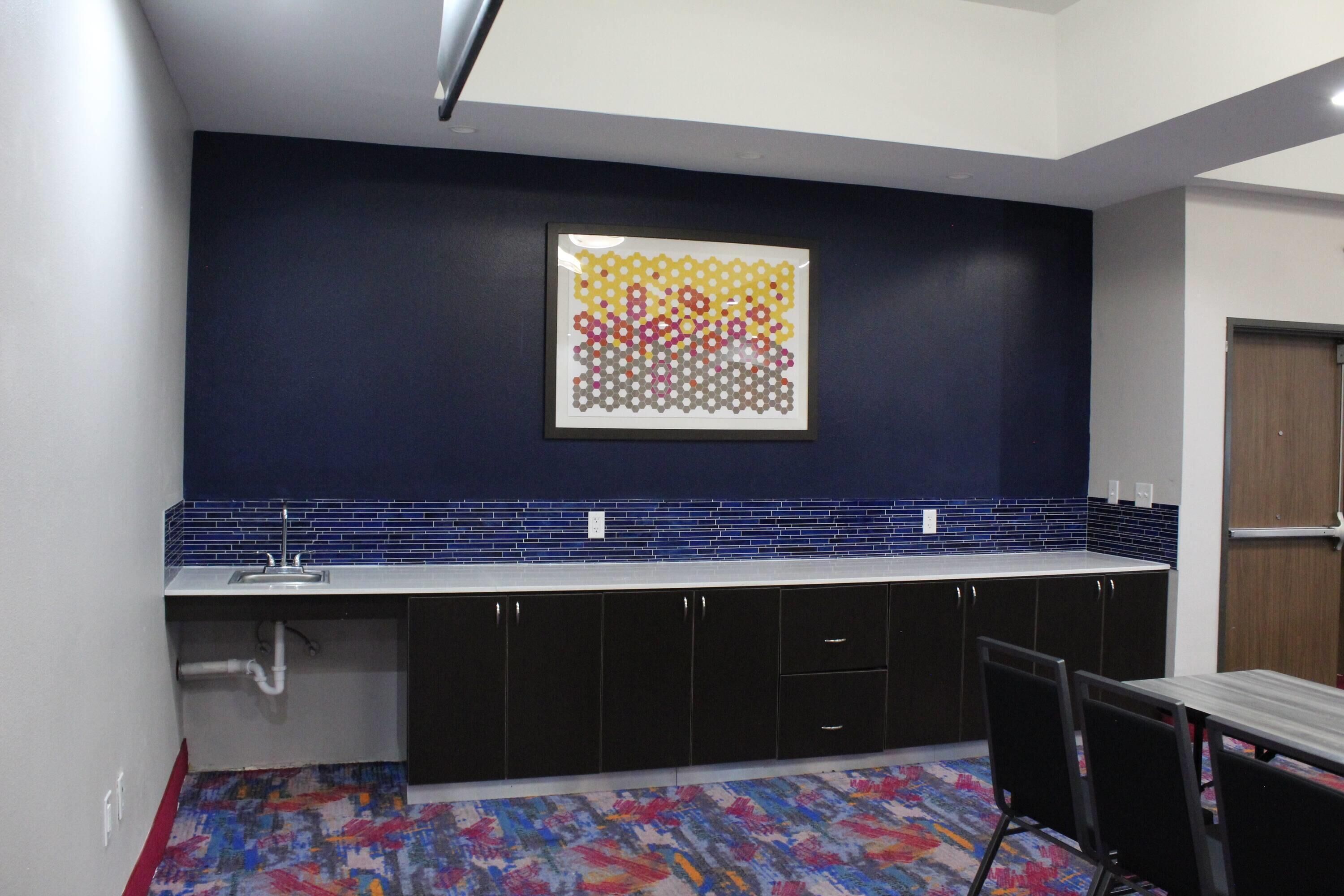 A kitchen with a blue backsplash, a colorful abstract art piece, and a patterned floor.