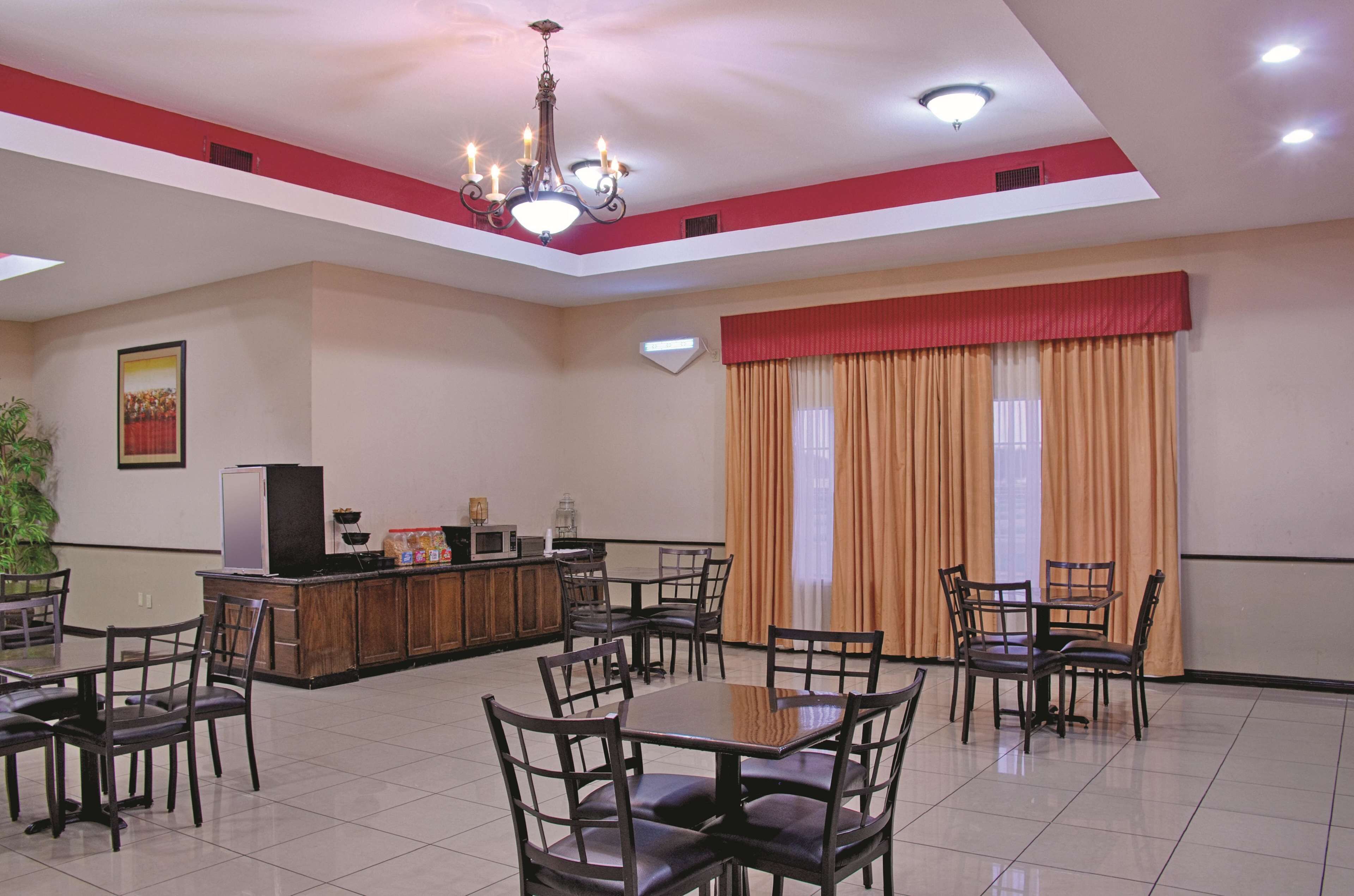 A spacious dining area with multiple tables and chairs, a kitchen counter with appliances, and a large window with curtains.