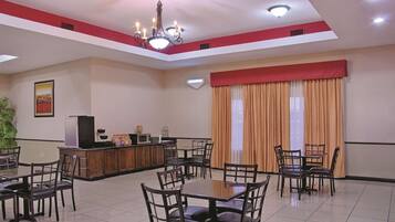 A spacious dining area with multiple tables and chairs, a kitchen counter with appliances, and a large window with curtains.
