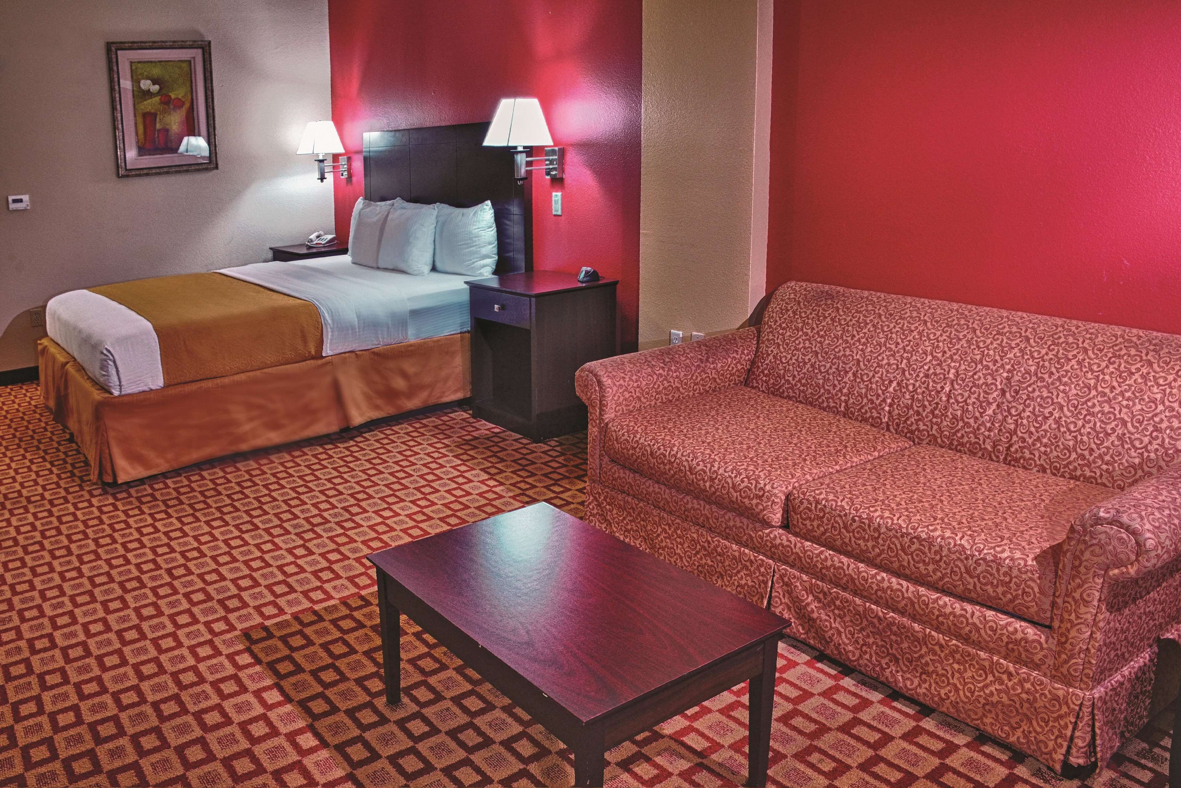 A hotel room with a bed, a sofa, a table, and a patterned carpet.