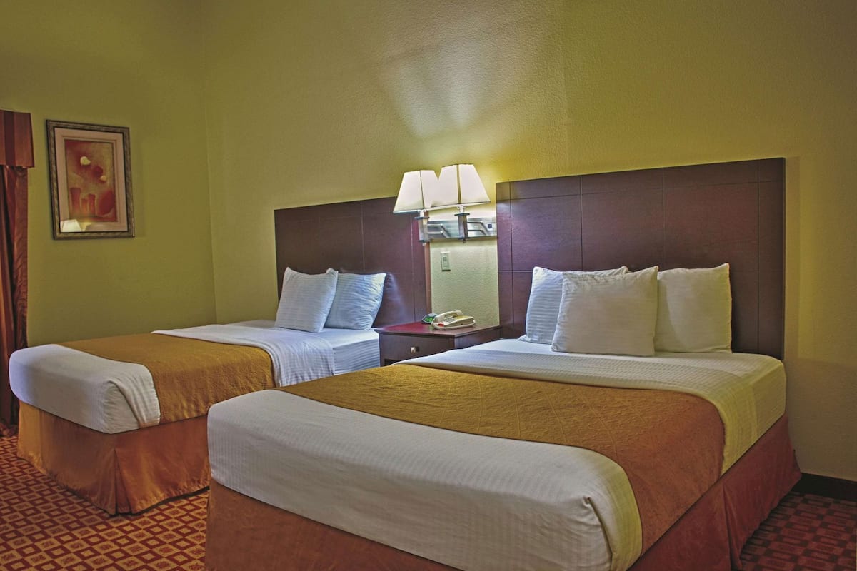 A hotel room with two beds, a nightstand with a lamp, and a painting on the wall.