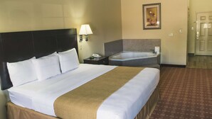 A hotel room with a large bed, a bedside table with a lamp, a small bathroom with a sink and mirror, and a framed picture on the wall. - La Quinta Inn & Suites by Wyndham Alice (Alice)