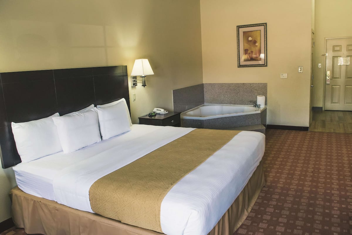 A hotel room with a large bed, a bedside table with a lamp, a small bathroom with a sink and mirror, and a framed picture on the wall.