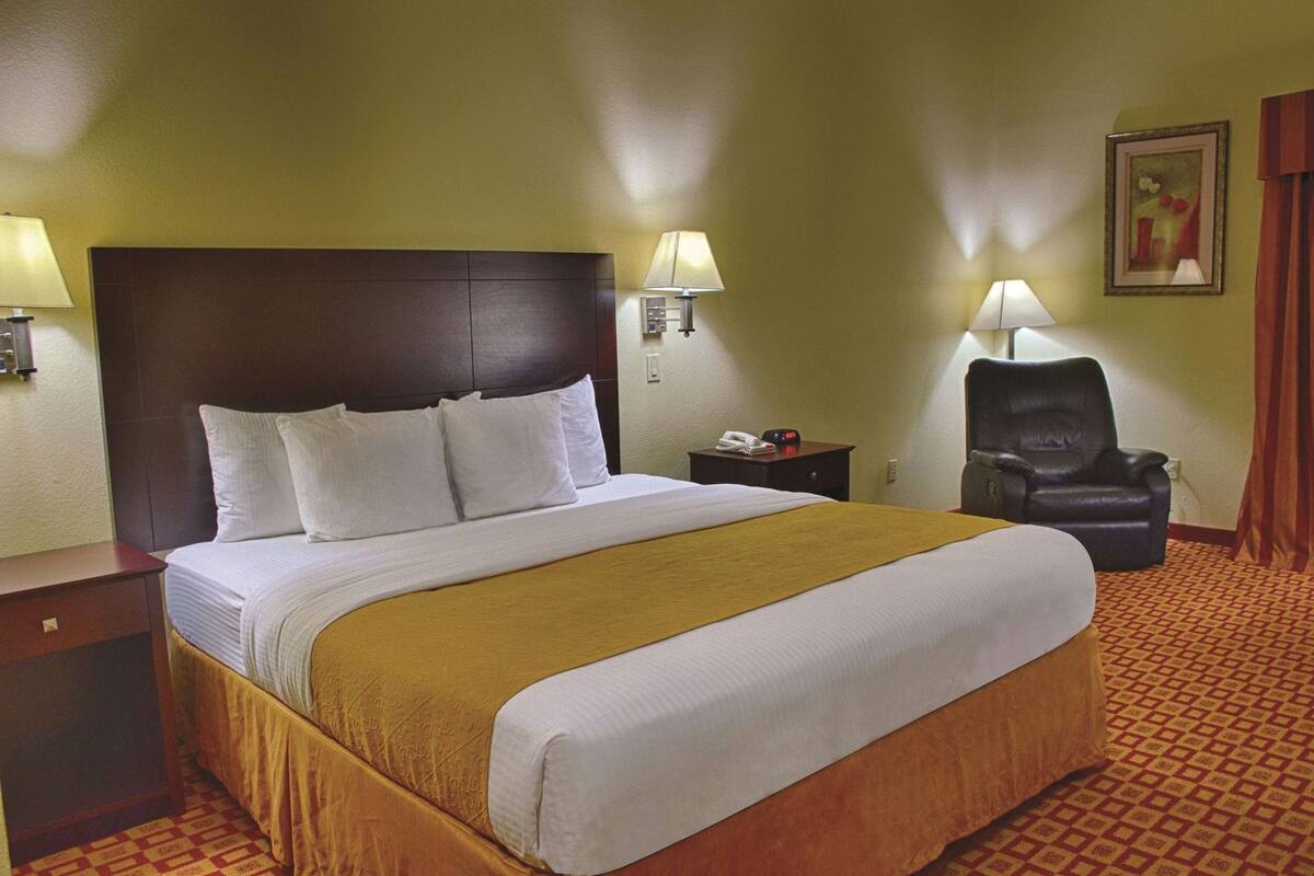 A hotel room with a large bed, bedside lamps, a chair, and a nightstand.