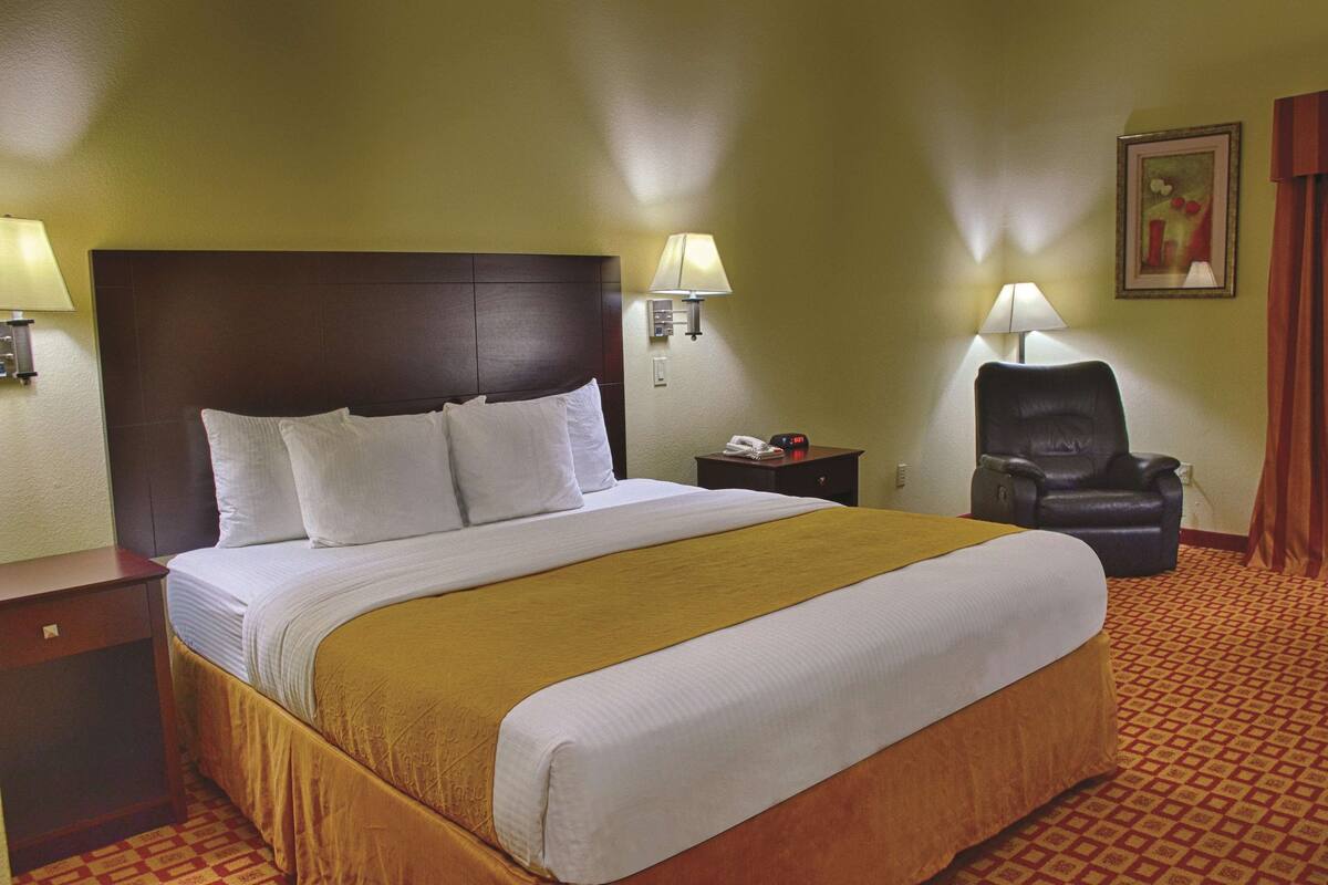 A hotel room with a large bed, two bedside lamps, a chair, and a painting on the wall.