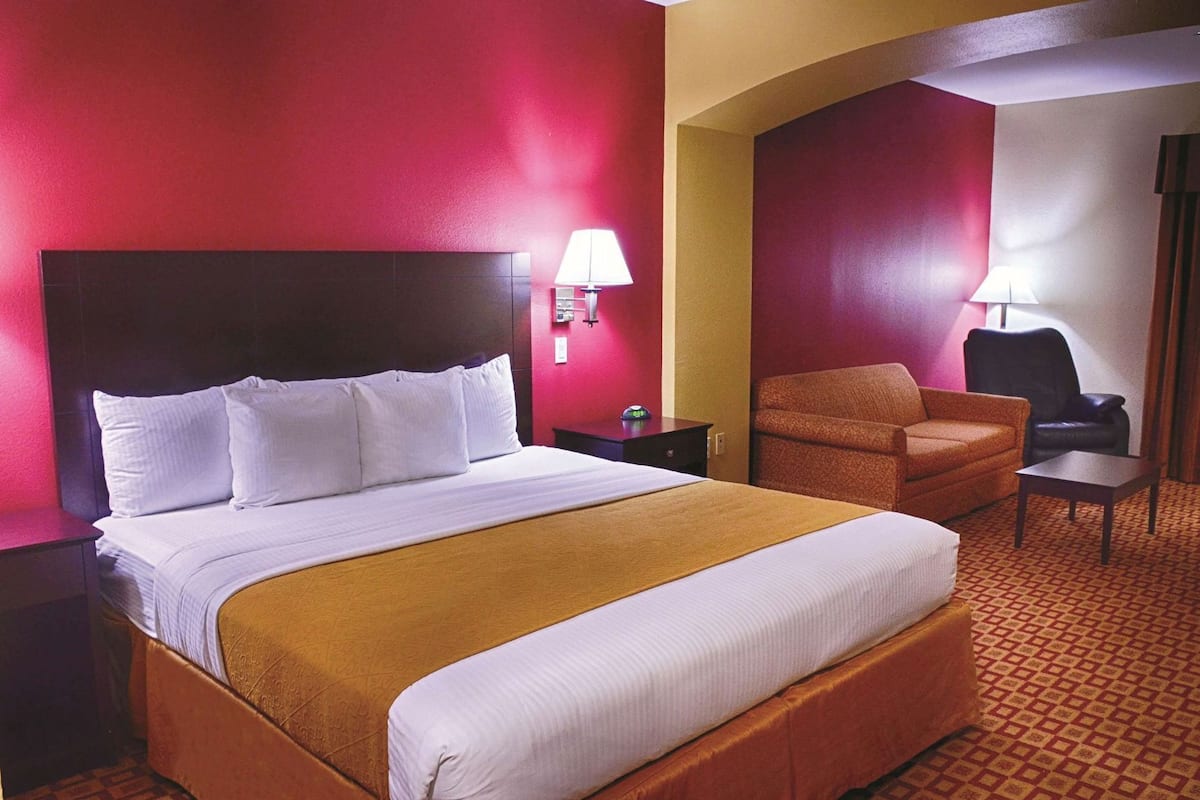 A hotel room with a large bed, a chair, a desk, and a lamp.
