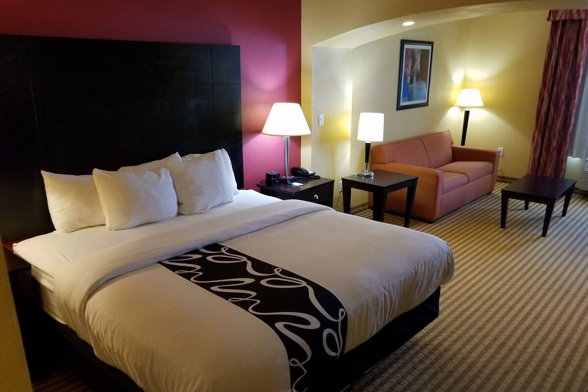 Una habitación de hotel con una cama grande, dos mesitas de noche, un sofá y dos lámparas.