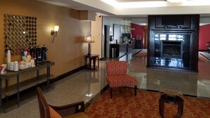 Vestíbulo de hotel con mostrador de recepción, un sillón estampado, estación de café, zona de cocina y chimenea.
