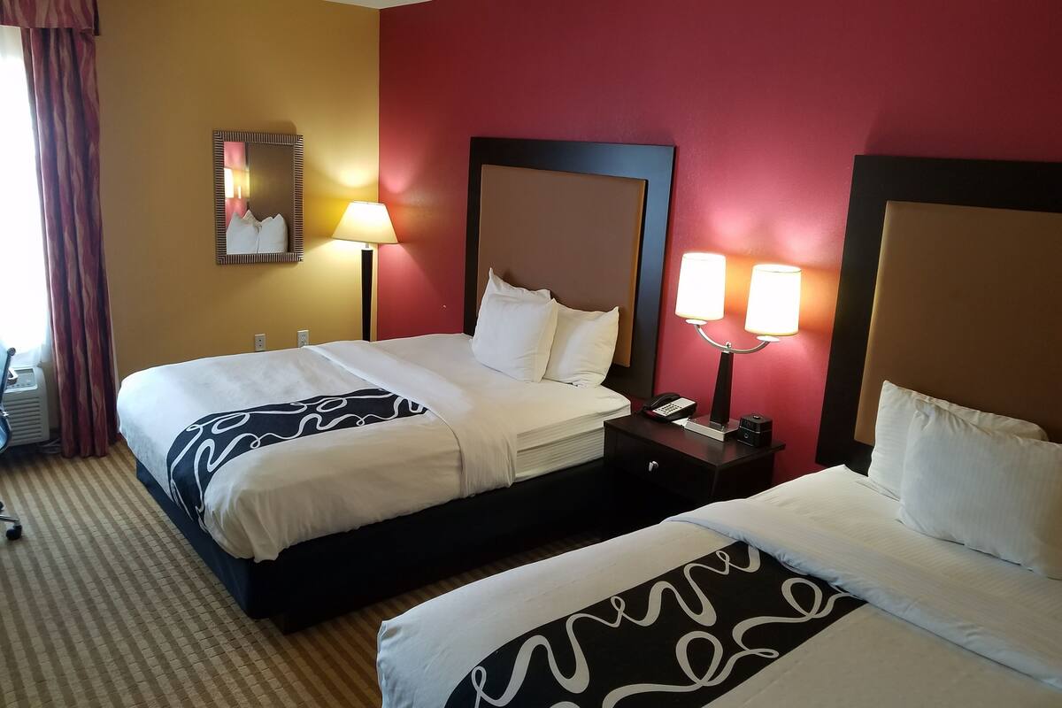 Habitación de hotel con dos camas, un espejo, lámparas de noche y una pared de acento roja.