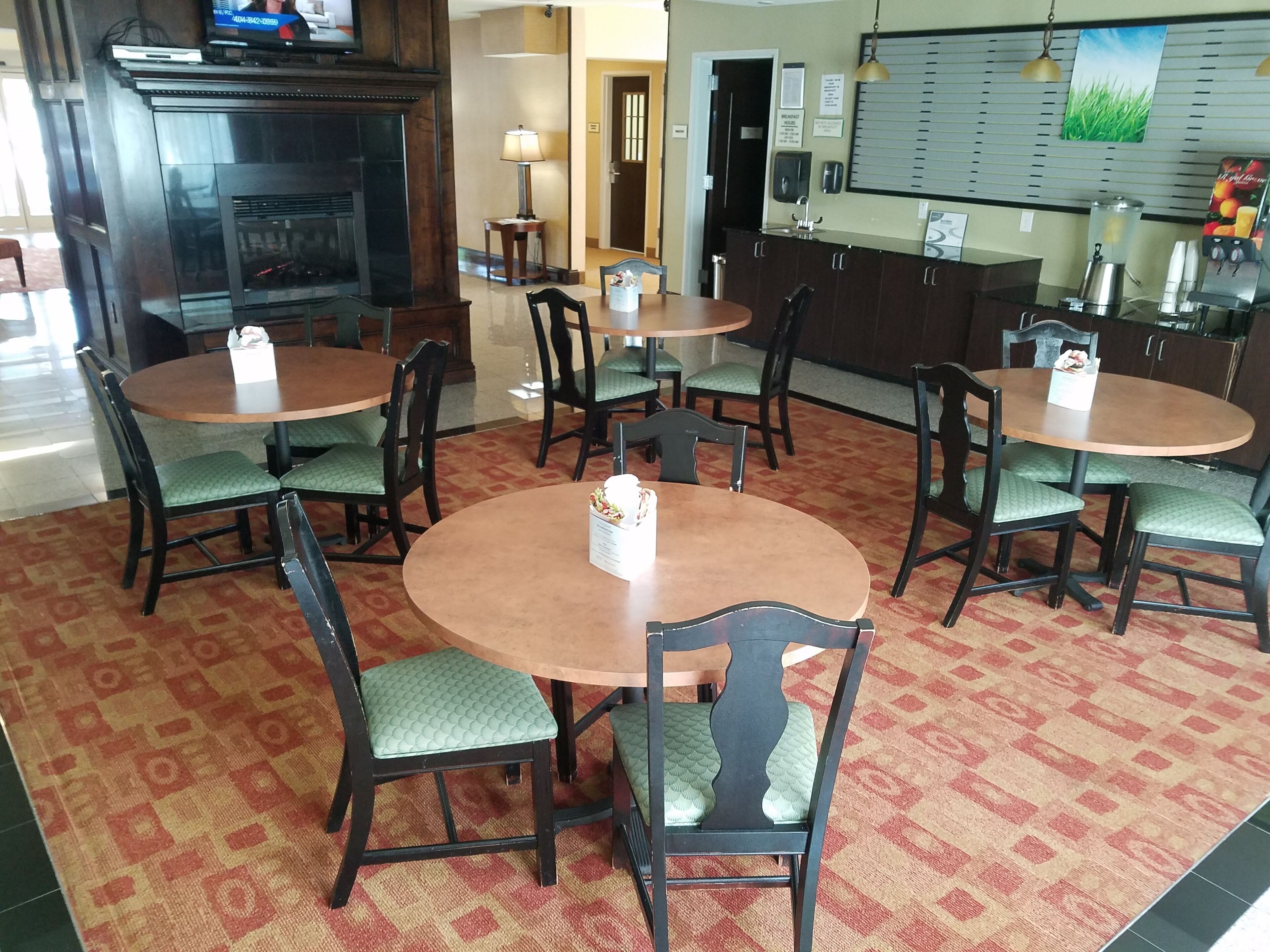 A hotel lobby with round tables and chairs, a reception desk, a fireplace, and a wall-mounted menu board.