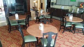 A hotel lobby with round tables and chairs, a reception desk, a fireplace, and a wall-mounted menu board.