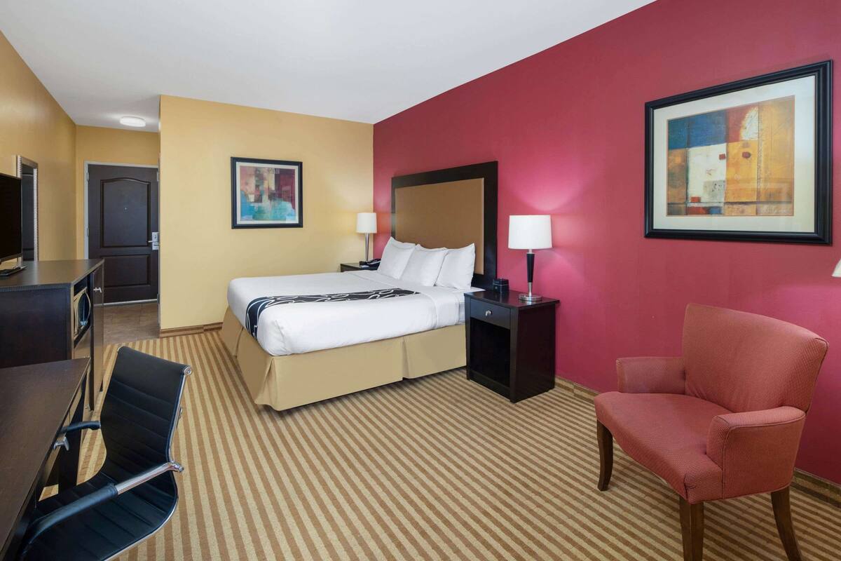 Una habitación de hotel con cama, escritorio, silla, televisor y obras de arte en las paredes.