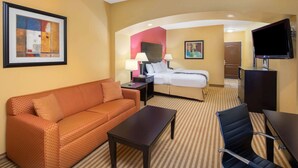Habitación de hotel con sofá, cama, escritorio, silla, televisor y un cuadro en la pared.