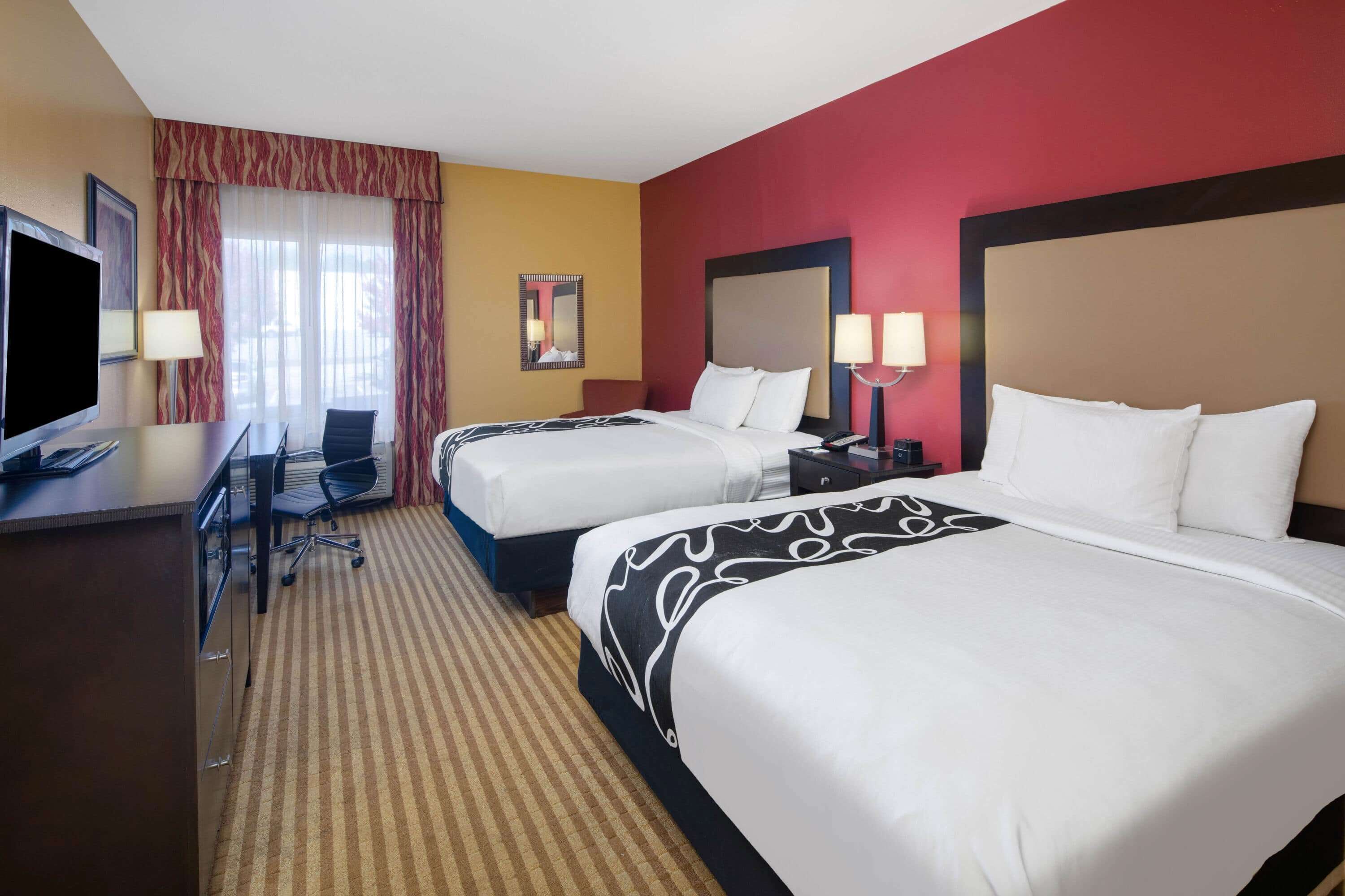 A hotel room with two beds, a desk with a TV, and a chair.